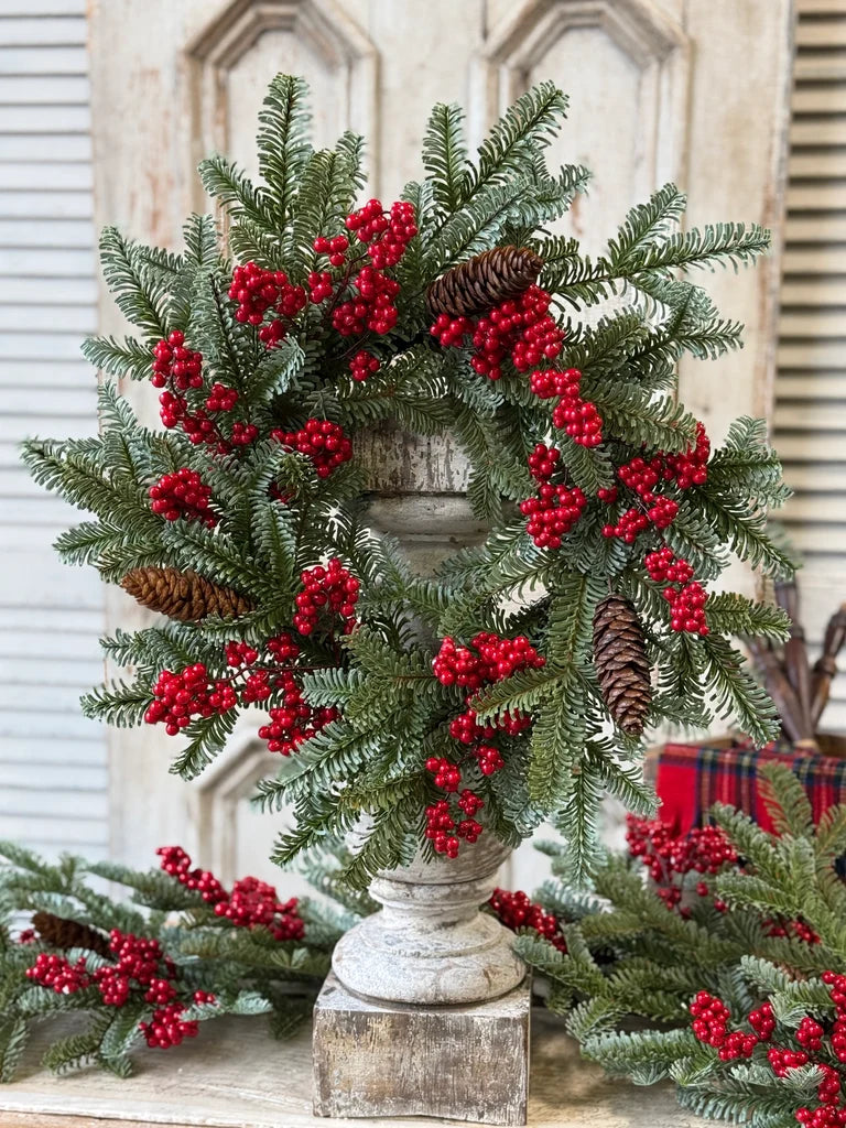 Christmas wreath with red berries and pine cones on a decorative stand.