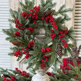 Christmas wreath with red berries and pine cones on a decorative stand.